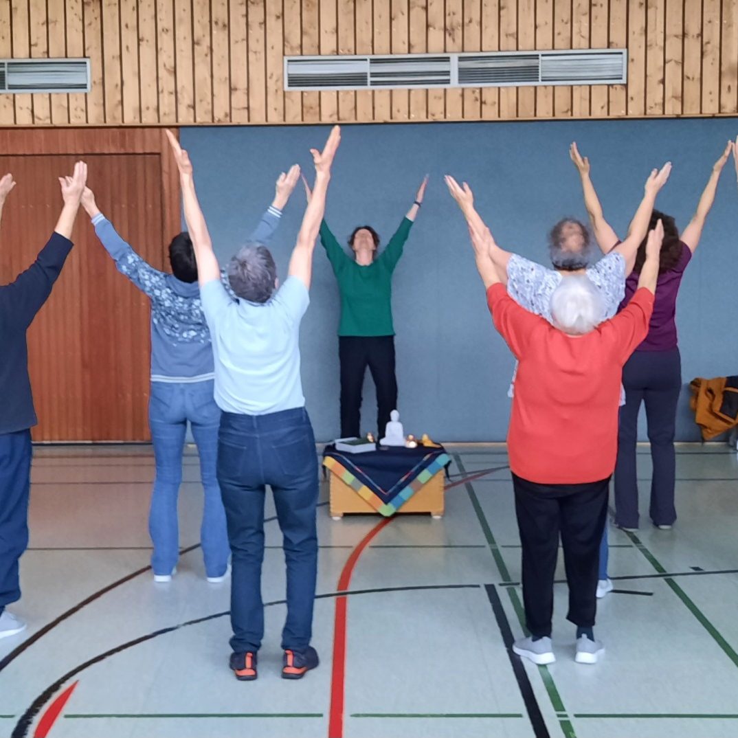 Gruppentraining in einer Sporthalle, Teilnehmer strecken die Arme nach oben.