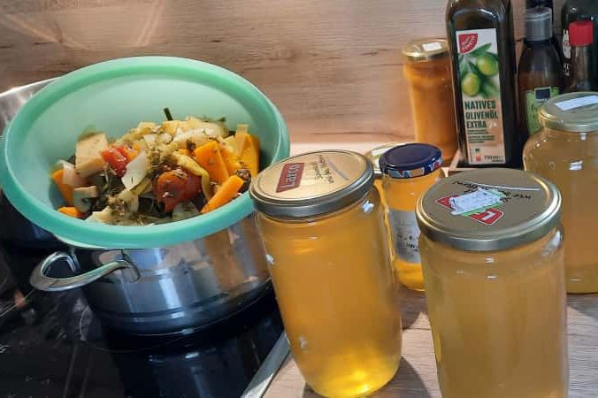 Ein Sieb mit Gemüse über einem Topf und Gläser mit Brühe.